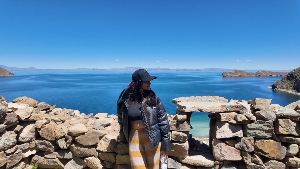 Mujer junto a muros de piedra en Isla del Sol, con el lago Titicaca al fondo