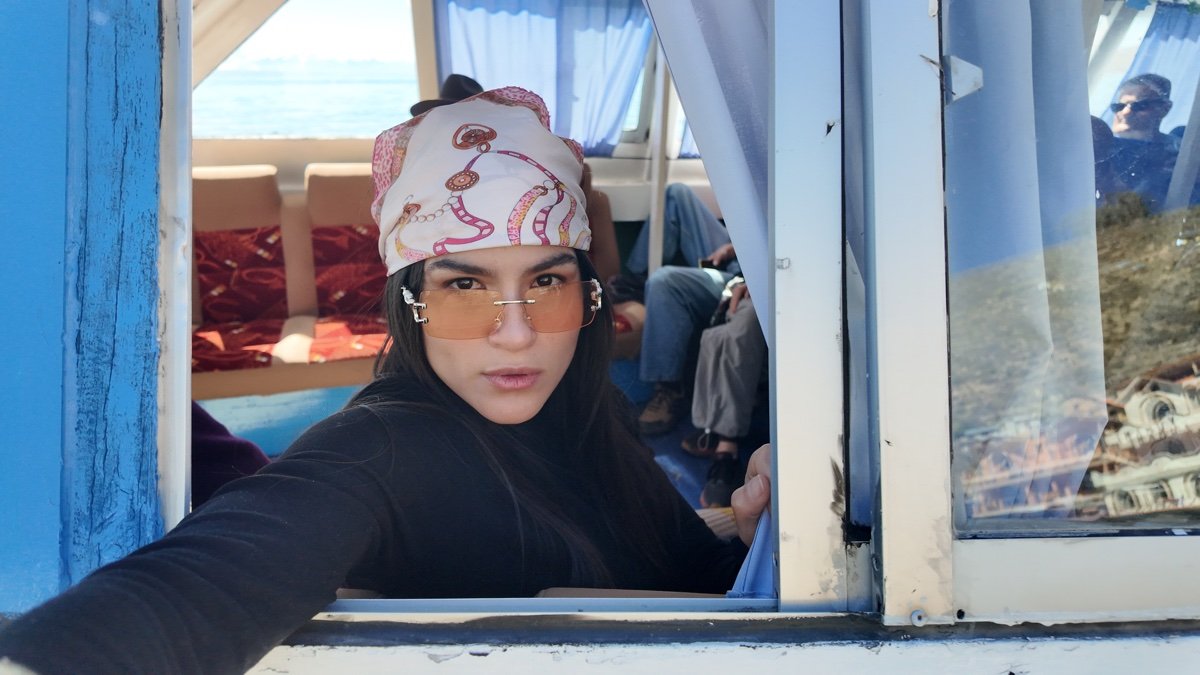 Mujer con gafas de sol y pañuelo asomada a la ventana de una embarcación