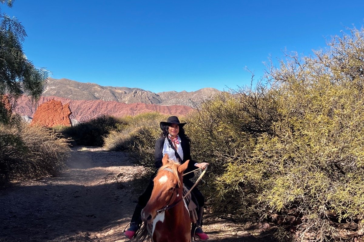 Dana recorre a caballo un sendero entre la vegetación y las montañas de Tupiza